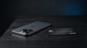 A modern smartphone on a dark desk next to a matte payment card